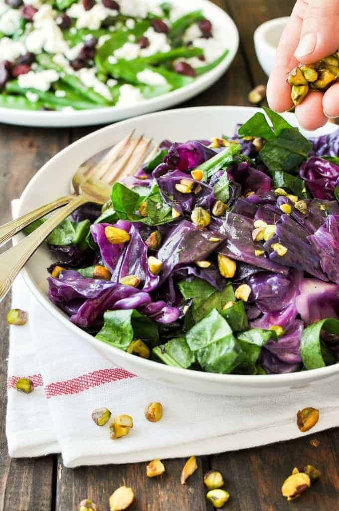 Sprinkling pistachio nuts on a Warm Red Cabbage Salad with Garlic Herb Butter in a white bowl.