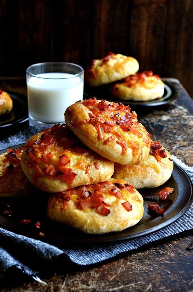 A pile of Double Cheese and Bacon Rolls with a glass of milk in the background