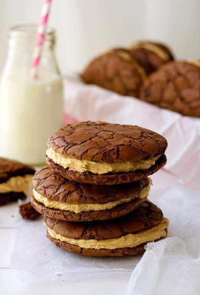 A pile of Brownie Cookie Sandwiches with Peanut butter Frosting, with milk in background