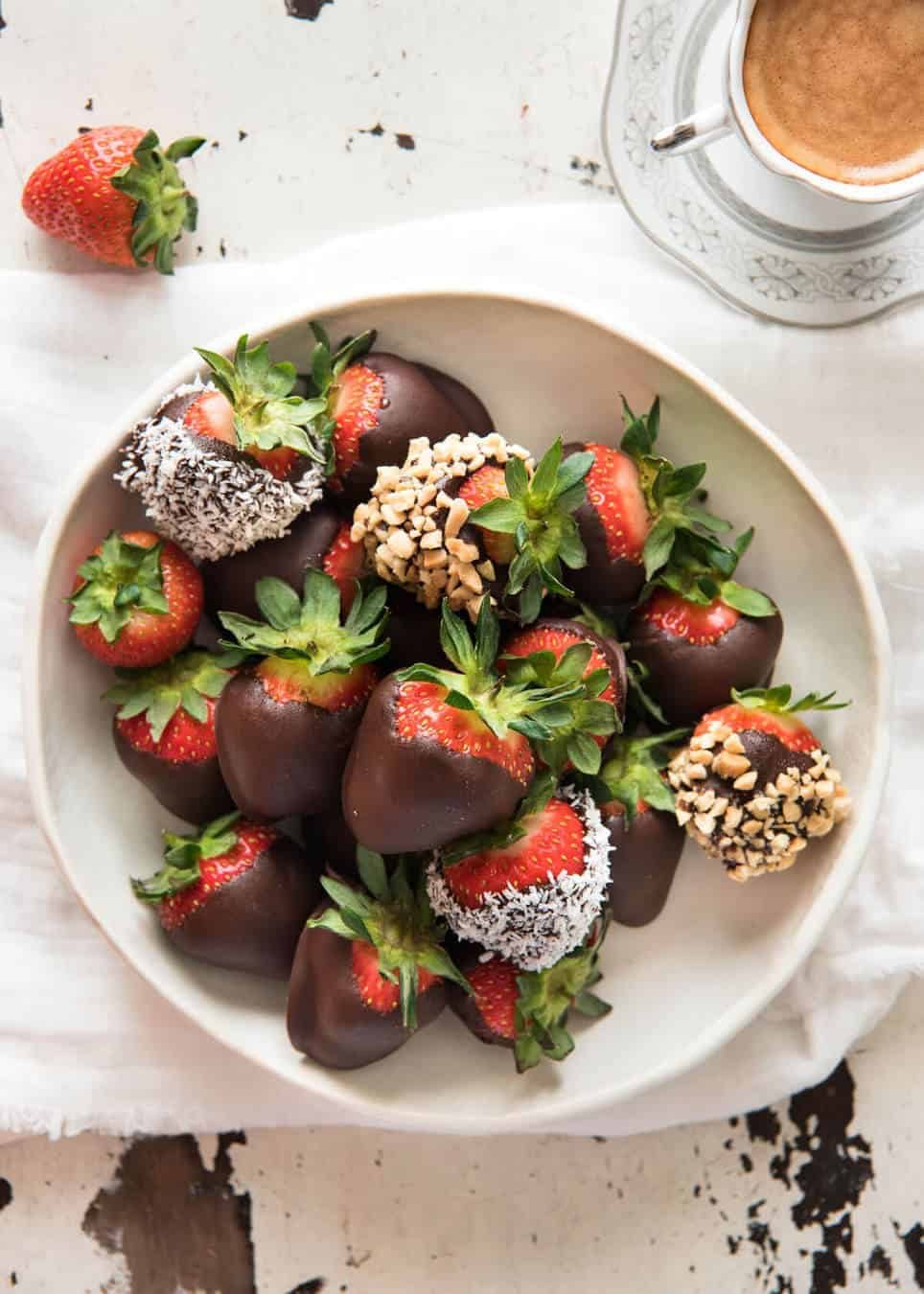 A bowl of chocolate covered strawberries, some coated in nuts and coconut.