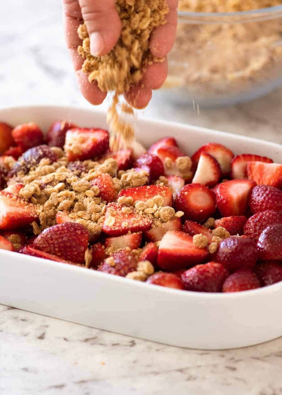 Sprinkling crumble topping on strawberries for Strawberry Crumble