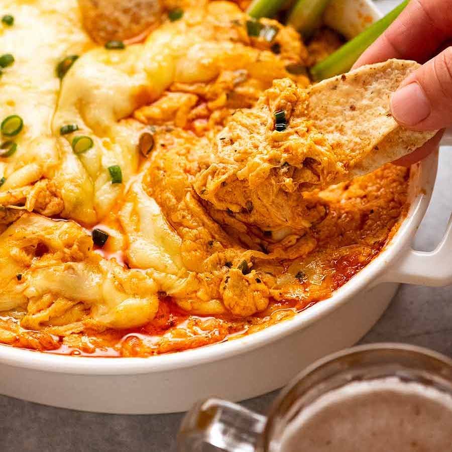 Close up scooping up Hot Buffalo Chicken Dip with corn chips